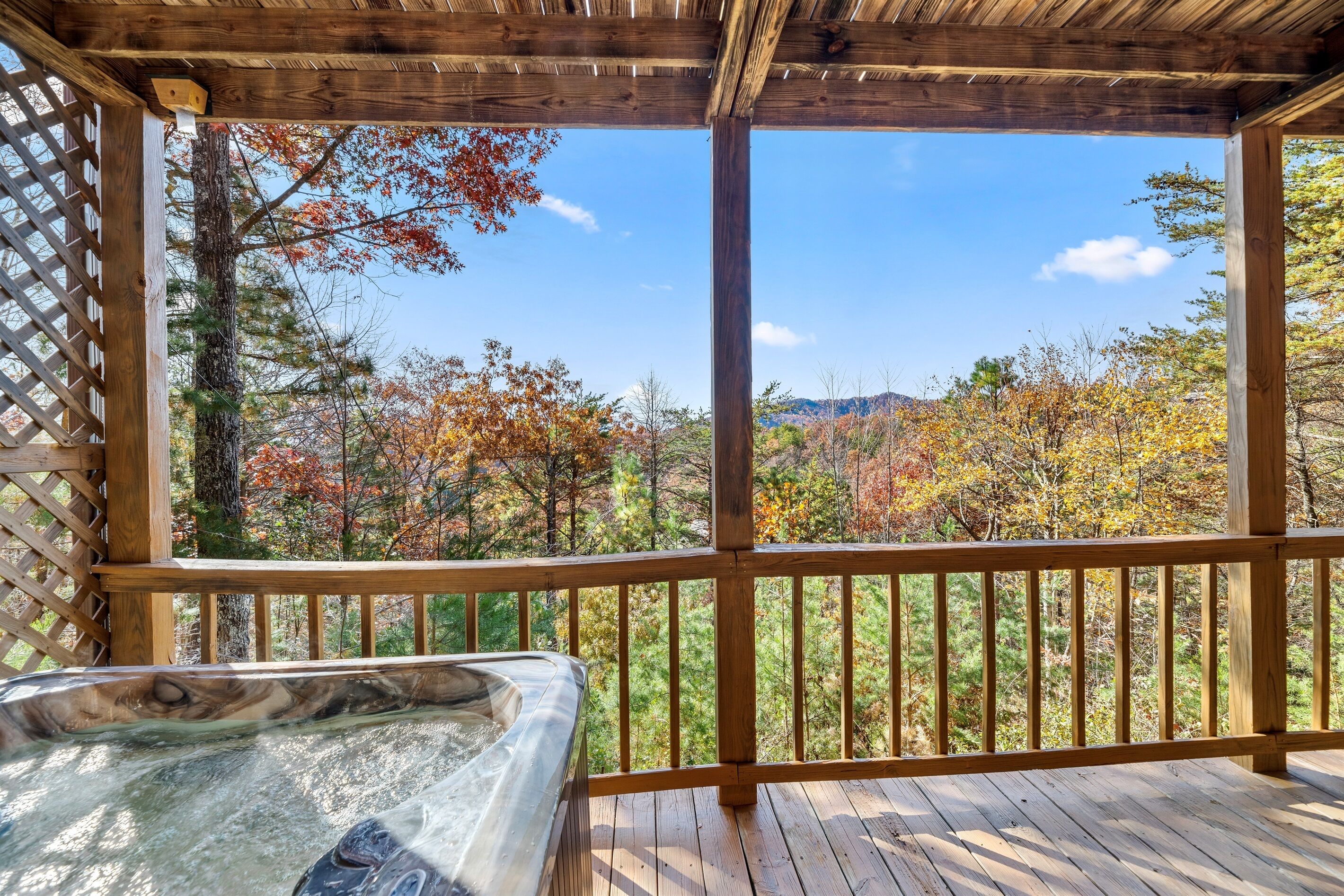 Une terrasse en bois avec un jacuzzi, donnant sur une zone boisée aux couleurs automnales.