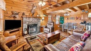 A cozy log cabin interior with a stone fireplace, leather furniture, and rustic decor. - Smokies Majestic Views | Hot Tub | Pool Table | Luxury Cabin (Sevierville)