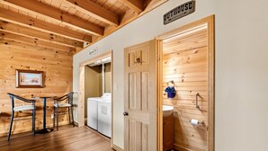 A wooden interior with a laundry area, a sign reading "Outhouse," and a small table with chairs. - Smokies Majestic Views | Hot Tub | Pool Table | Luxury Cabin (Sevierville)