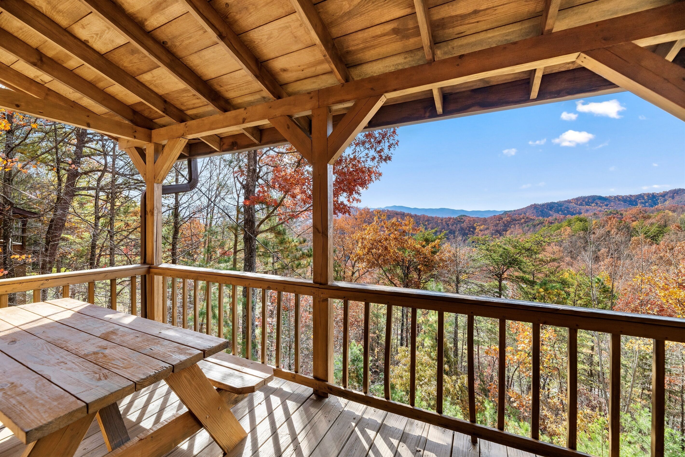 A wooden deck with a picnic table and a view of a forested mountain range.