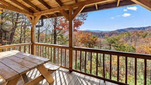 A wooden deck with a picnic table and a view of a forested mountain range. - Smokies Majestic Views | Hot Tub | Pool Table | Luxury Cabin (Sevierville)