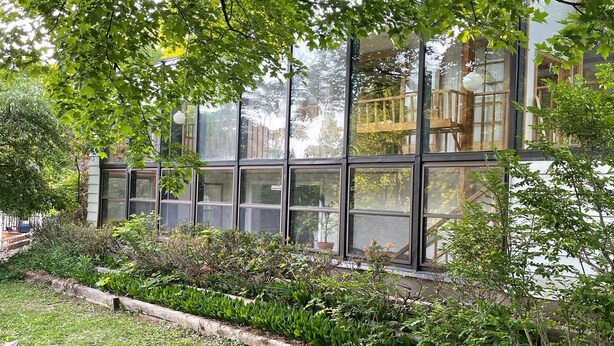 Ein modernes Gebäude mit großen Fenstern, umgeben von üppiger Bepflanzung und einem gepflegten Garten.