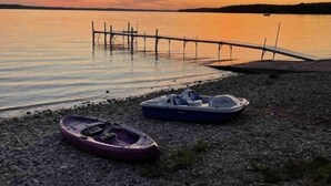 Ein Kiesstrand mit zwei Booten und einer hölzernen Anlegestelle, die sich in ruhiges Wasser bis zum Sonnenuntergang erstreckt.