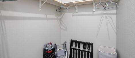 A storage closet with shelves, a black baby crib, and a laundry basket.