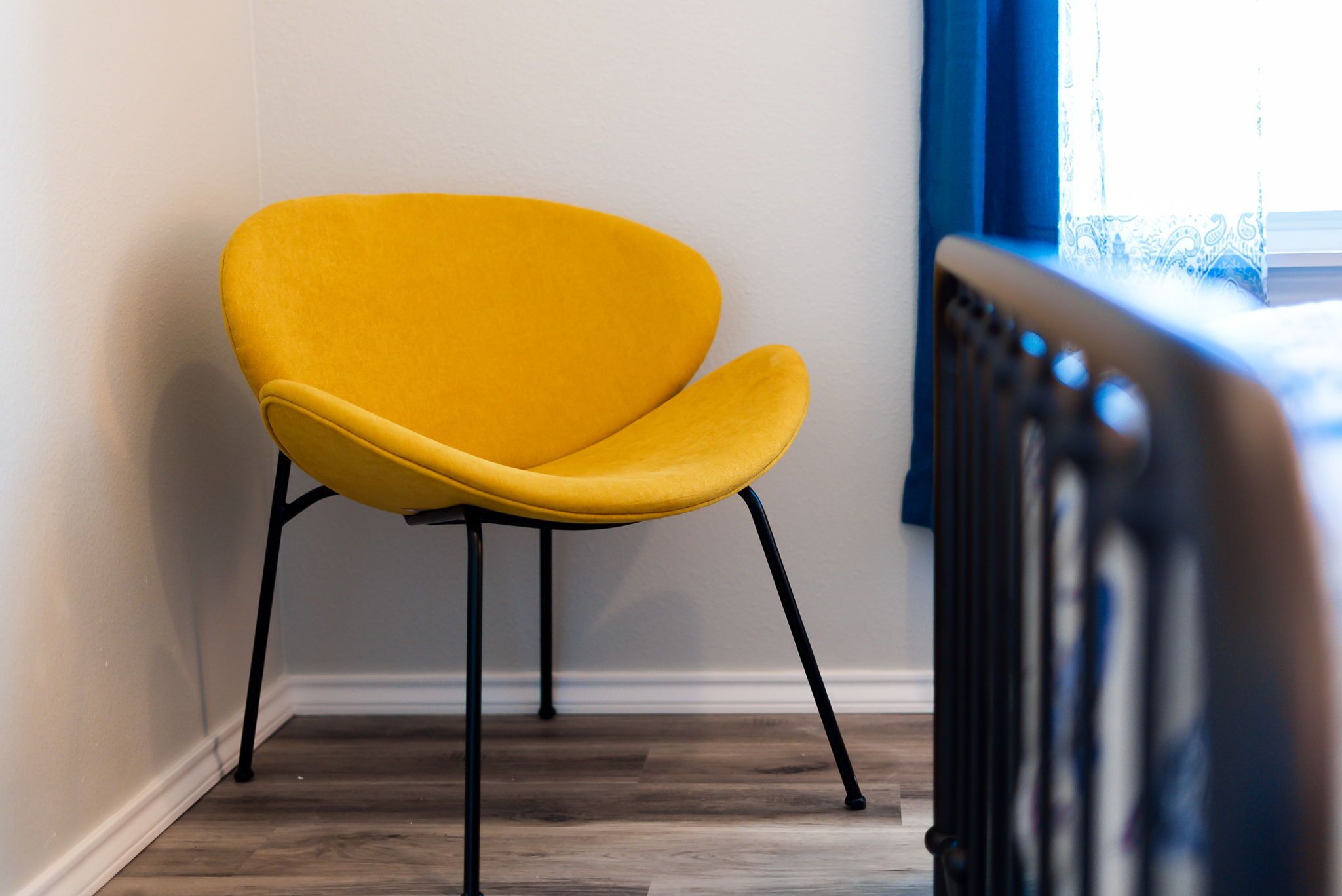 A yellow chair with black legs in a corner of a room with wooden flooring and a radiator.