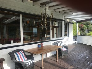 A covered porch with a wooden table and two wicker chairs with striped cushions. - Bluff Hill Lighthouse B&B (Napier)