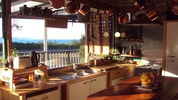 Cocina con una isla grande, vistas al exterior y diversos utensilios de cocina colgando.