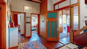 Un pasillo espacioso con pisos de madera, un tapete estampado y una puerta que da a una habitación con una silla roja y una mesita.