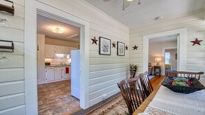 A dining area with a wooden table and chairs, a kitchen in the background, and decorative stars on the wall. - Historic Carriage House - Downtown Waynesville, Walk to Main Street! Fast Wifi! (Waynesville)