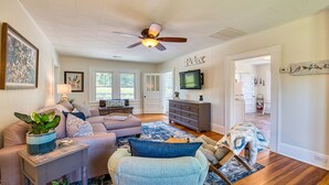 A spacious living room with a ceiling fan, a television, and a large window. - Historic Carriage House - Downtown Waynesville, Walk to Main Street! Fast Wifi! (Waynesville)