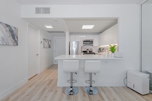 A modern kitchen with a central island, two bar stools, a microwave, a refrigerator, and a stove. - Luxury Oceanfront resort/condo/1 Hotel / Roney Palace (Miami Beach)
