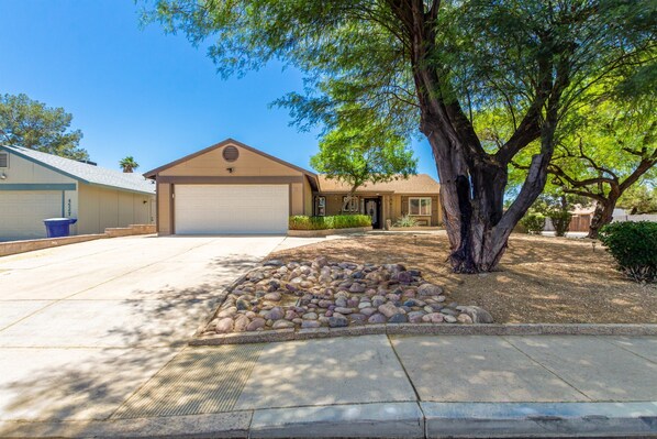 A single-story house with a garage, a stone patio, and a large tree in front. - Fall Special! Private Pool/Spa! (Chandler)
