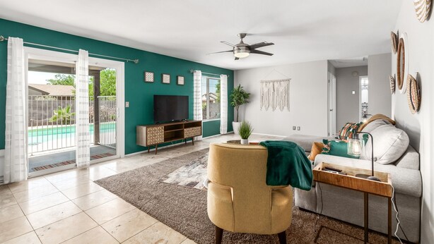 A spacious living room with a teal accent wall, a ceiling fan, a TV, a sofa, and a coffee table. - Fall Special! Private Pool/Spa! (Chandler)