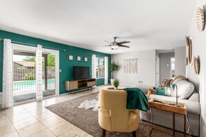 A spacious living room with a teal accent wall, a ceiling fan, a TV, a sofa, and a coffee table. - Fall Special! Private Pool/Spa! (Chandler)