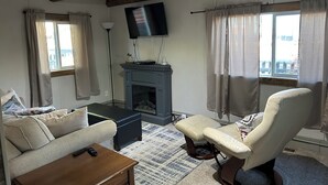 Un salon avec une cheminée, un canapé, un fauteuil et un téléviseur fixé au mur.