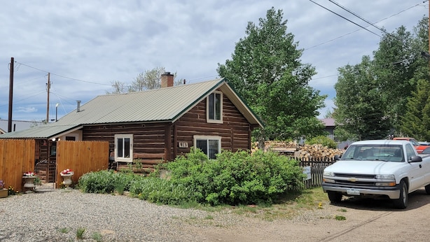 Une cabane en rondins de bois, avec une allée en gravier et un camionnette blanche garée devant.