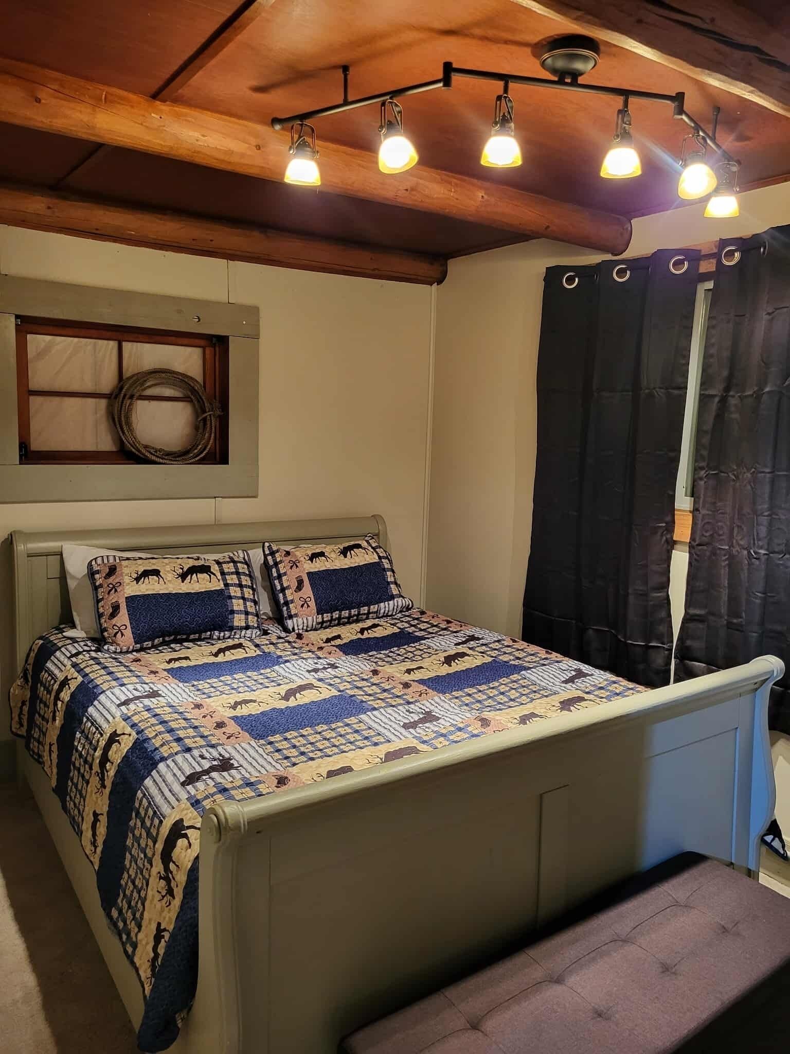 A bedroom with a bed, a bench, a wooden ceiling, and a window with curtains.