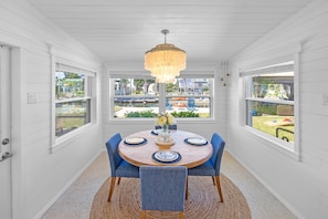 A dining area with a round table, blue chairs, a chandelier, and large windows with a view of the outdoors.