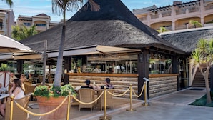 Un resort con área de bar de techo de paja, asientos exteriores y un lounge junto a la piscina.