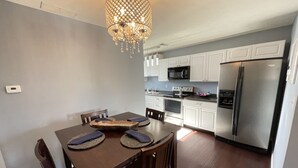 Une cuisine moderne avec des meubles blancs, des appareils en acier inoxydable et un coin repas comprenant une table et des chaises en bois.
