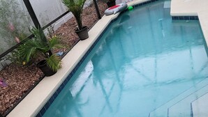 Ein Schwimmbecken mit gefliestem Rand, umgeben von einer Betonplattform und Blumentöpfen.