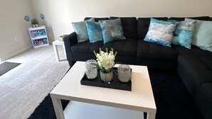 Ein modernes Wohnzimmer mit einer schwarzen Couch, einem weißen Couchtisch und einem Gemälde eines Sonnenuntergangs.
