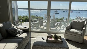 A sunlit living room with a large sliding glass door leading to a deck overlooking a marina with boats. - Brand new private  beachfront home in Mashpee on Waquoit Bay (Mashpee)