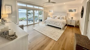 A bedroom with a large bed, a ceiling fan, a nightstand, and a view of the outdoors. - Brand new private  beachfront home in Mashpee on Waquoit Bay (Mashpee)