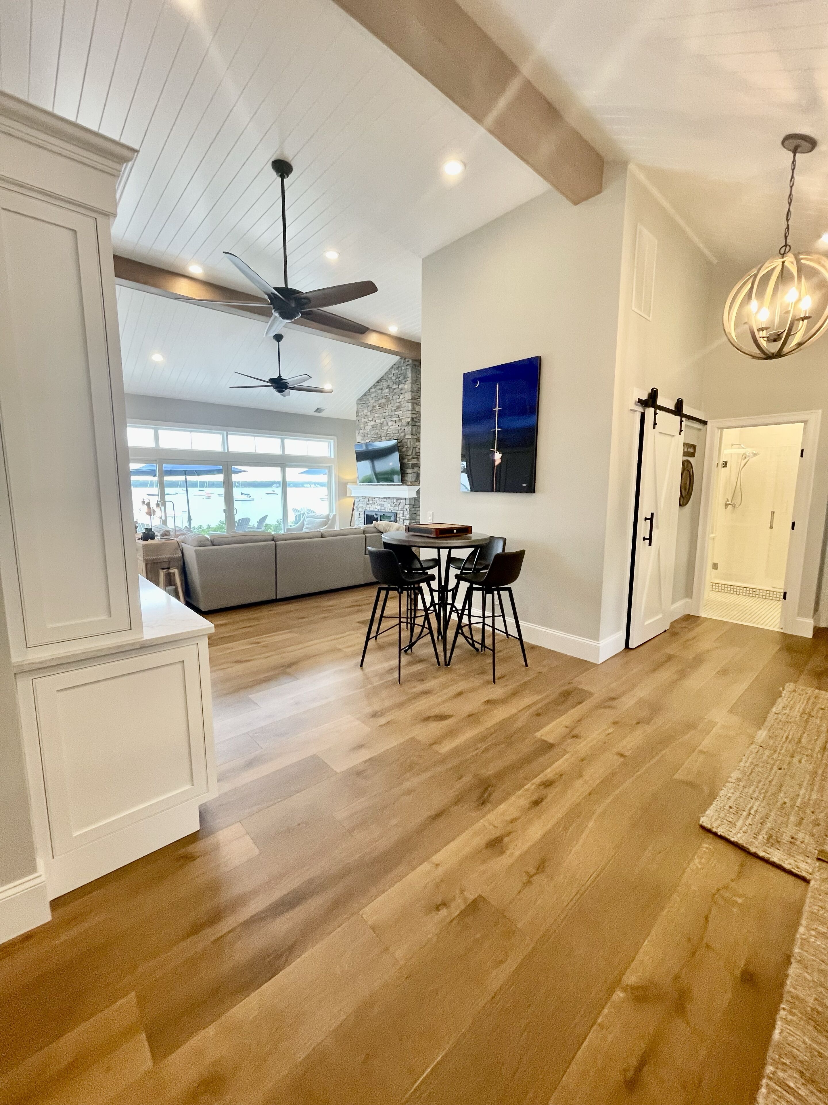A spacious living area with hardwood flooring, a dining table with chairs, a fireplace, and a large window overlooking a marina.