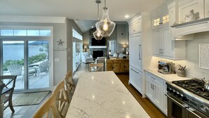 A spacious kitchen with a large island, white cabinetry, and a view of the ocean through the sliding glass doors. - Brand new private  beachfront home in Mashpee on Waquoit Bay (Mashpee)