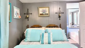Un dormitorio con dos camas de madera, un cuadro en la pared y dos lámparas fijadas a la pared.