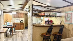 Cocina compacta con armarios de madera, comedor con mesa y sillas, y barra con taburetes.