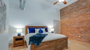 Een slaapkamer met een houten bed, twee nachtkastjes, een bakstenen muur en een plafondventilator.
