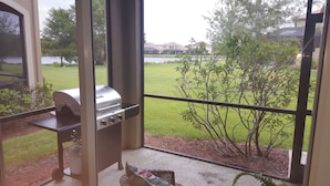 A view from a window overlooking a backyard with a barbecue grill, a small tree, and a grassy lawn. - Welcome to your South West Florida Paradise! (Estero)