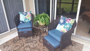 A patio area with wicker chairs and a table, a potted fern, and a view through a glass door. - Welcome to your South West Florida Paradise! (Estero)
