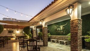 Un patio al aire libre con pilares de piedra, sillas de madera y una pared con el letrero de un restaurante.