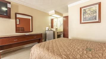 Ein Hotelzimmer mit einem Bett, einem Holzschrank, einem Spiegel, einem Kühlschrank und einem gerahmten Bild an der Wand.