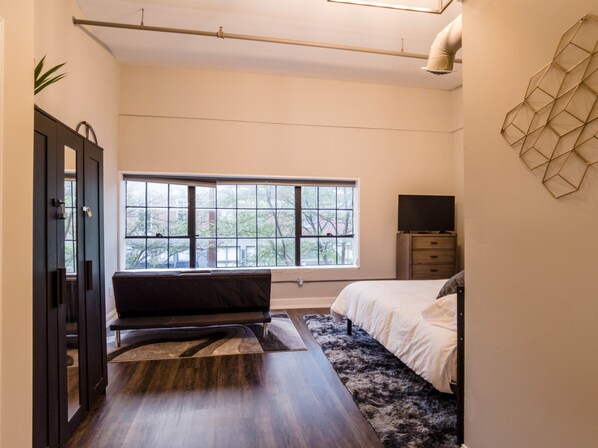 Ein modernes Schlafzimmer mit großem Fenster, einem Bett, einer Bank, einem Fernseher und einer Wanddekoration.