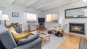 Ein Wohnzimmer mit einer Couch, Sesseln, einem Couchtisch, einem Kamin und einem Fernseher.