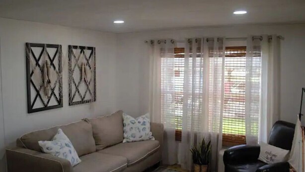 A living room with a beige sofa, two decorative wall pieces, a black leather chair, and a window with sheer curtains. -  Canal  access to the St. Johns River. Private boat dock. Parking for  trailer (Welaka)