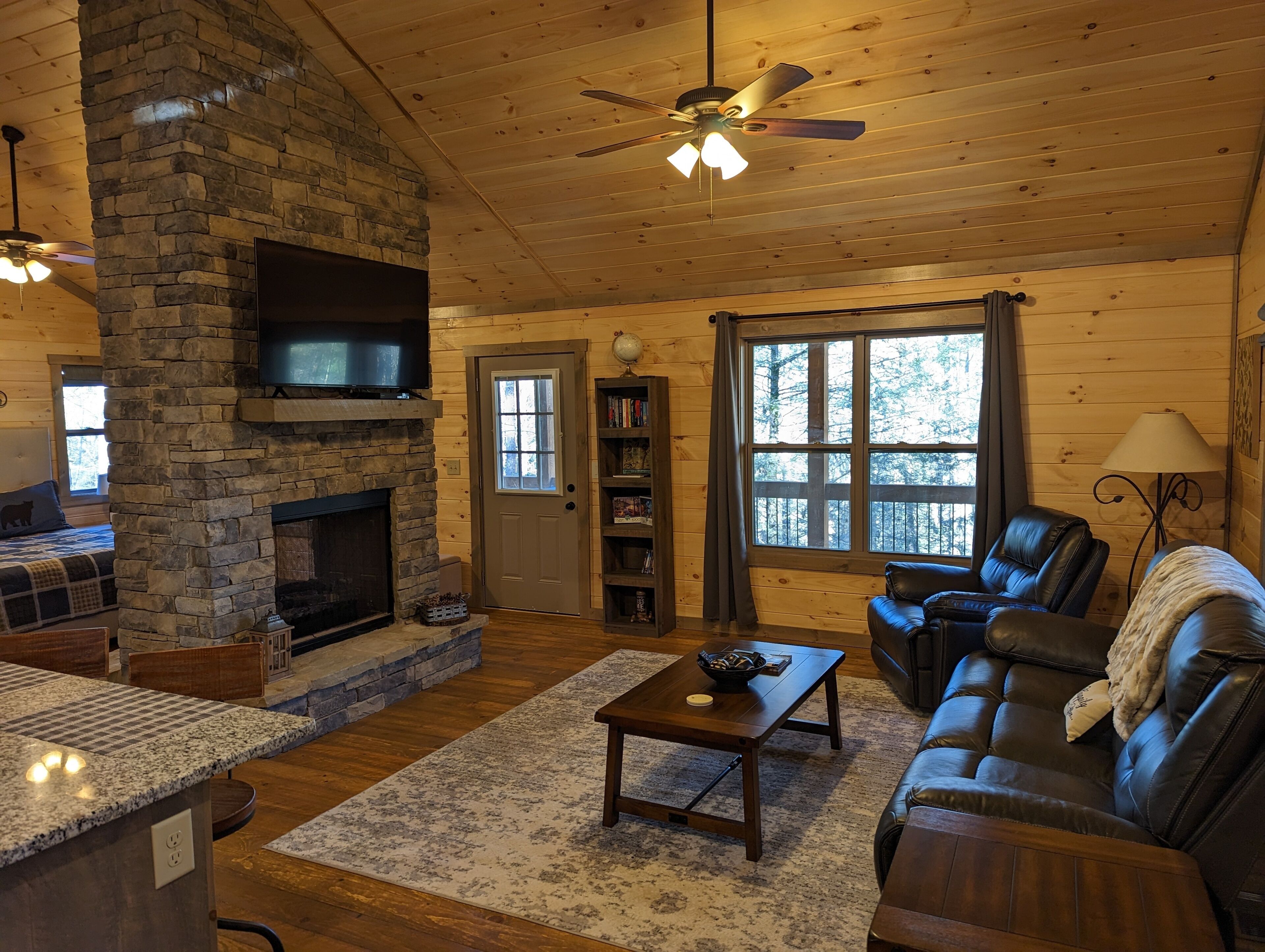 A cozy cabin interior with a stone fireplace, wooden ceiling, and a comfortable seating area.