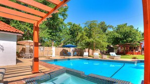 Una piscina con hidromasaje, rodeada de sillas de descanso y sombrillas, con una terraza de madera y una pérgola.