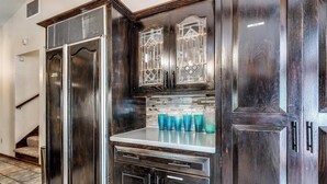 Una cocina de madera oscura con estufa empotrada, despensa con puerta de vidrio y salpicadero de azulejos.