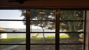 Une vue à travers une fenêtre donnant sur une étendue d’eau, un quai et une zone herbeuse.