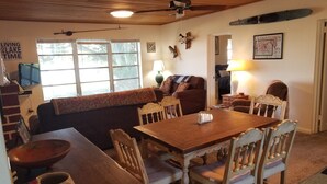 Un salon chaleureux avec une table à manger en bois, des sièges confortables et un téléviseur fixé au mur.