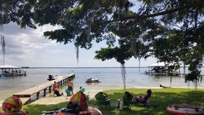 Un cadre idyllique au bord d’un lac, avec un quai, des bouées gonflables et des gens qui se détendent sur l’herbe.