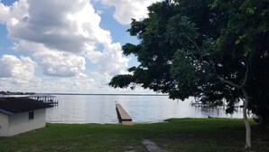 Une vue sur le lac avec une jetée s’avançant dans l’eau, une zone herbeuse et un bâtiment doté d’un espace de repos abrité.