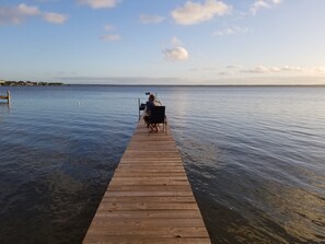 A wooden pier extending into calm water with a person seated at the end. - Lakefront getaway with white sand, clear water, gorgeous sunsets (Lake Placid)