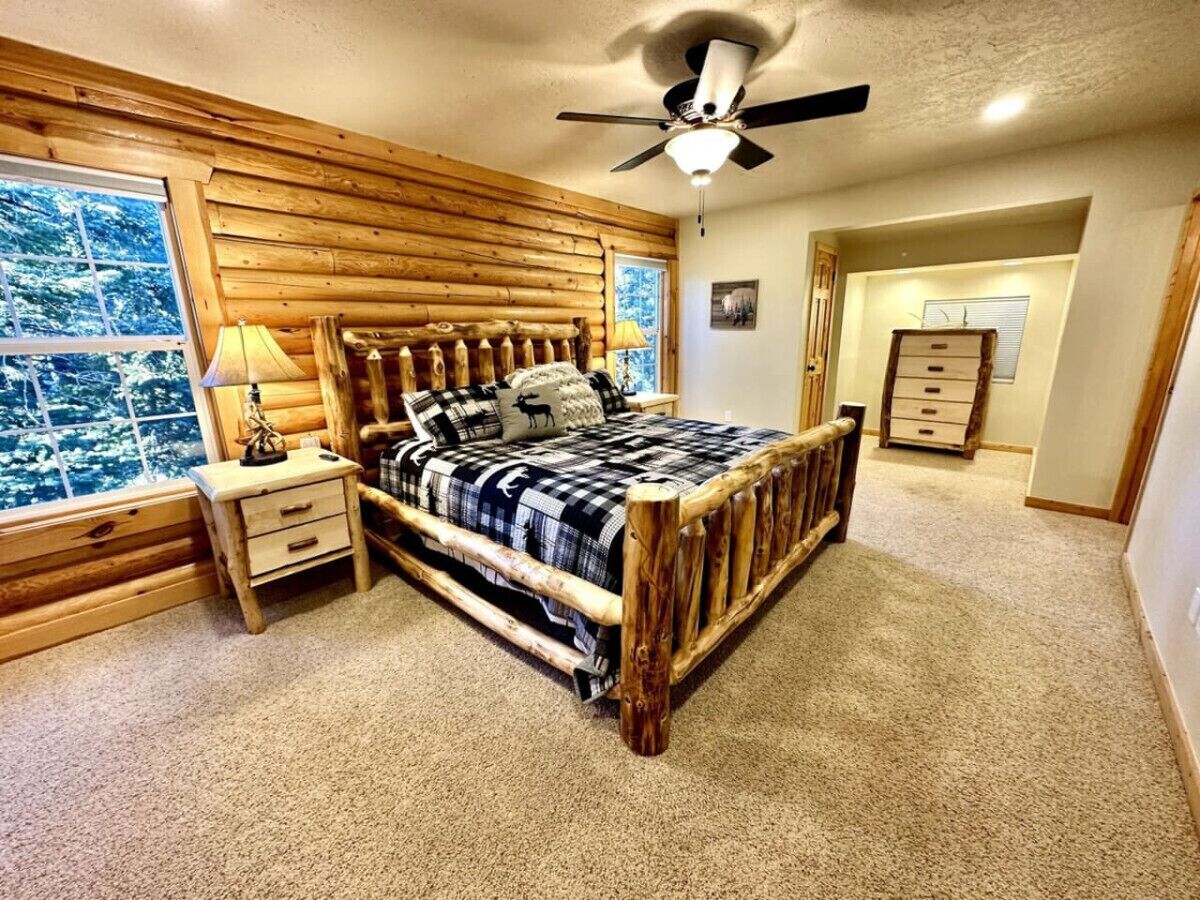 A bedroom with a wooden bed, a nightstand, a lamp, and a window with a view of trees.