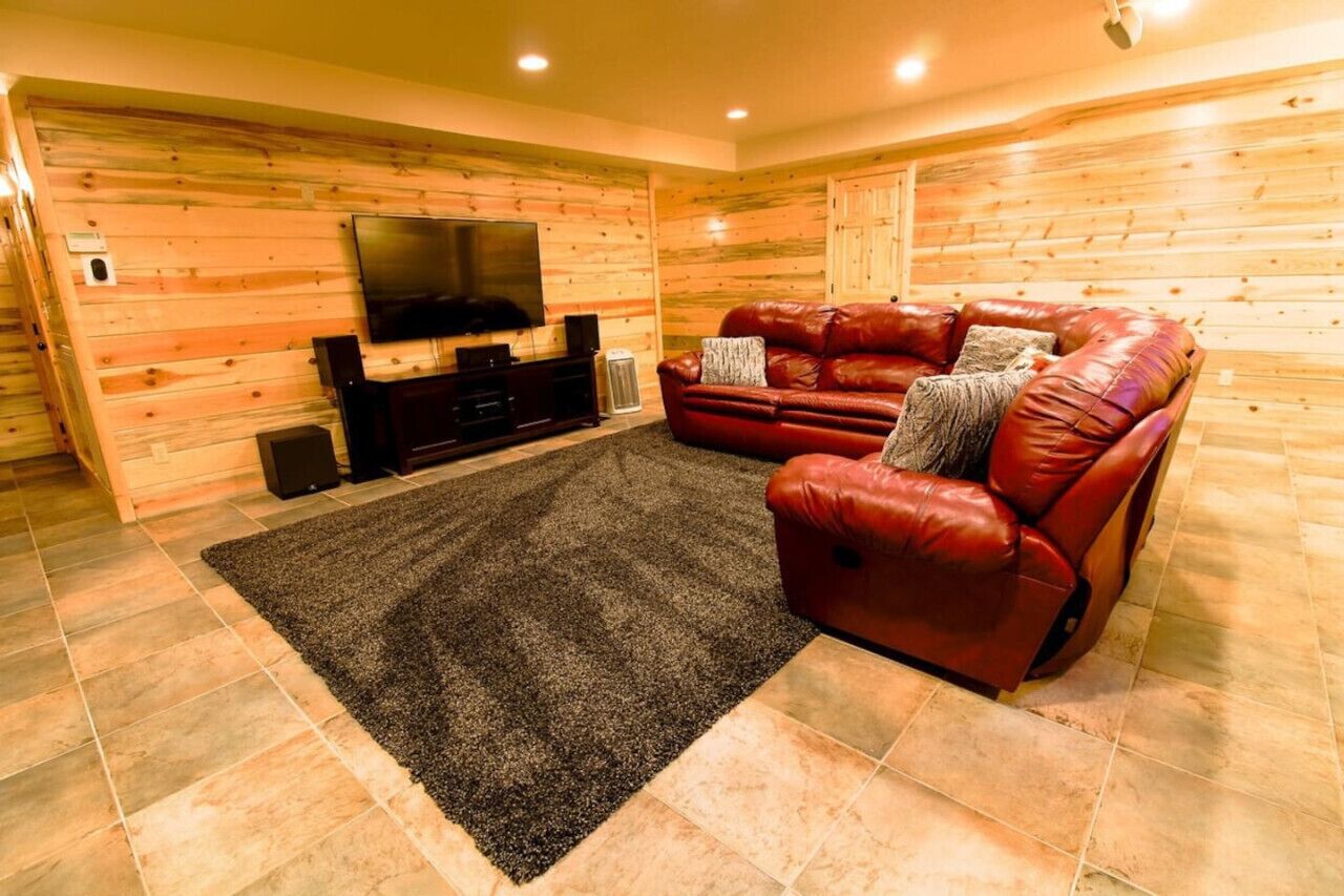 A cozy living room with a leather sofa, a flat-screen TV, and a dark rug on a tiled floor.